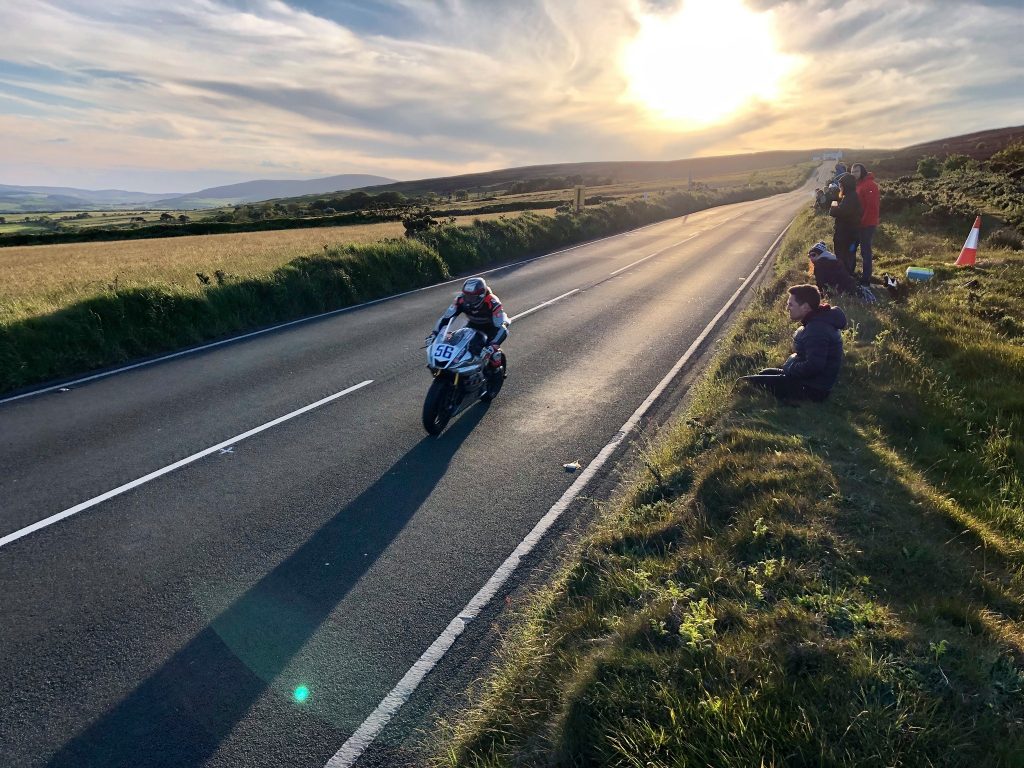 View of an Isle of Man TT rider blasting along the road with the sun setting behind